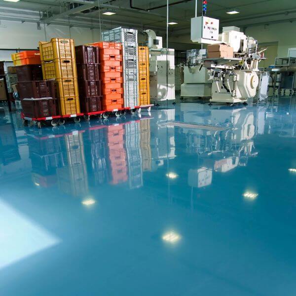Shiny blue epoxy floor in a busy industrial workspace with crates and machinery, installed by Epoxy Flooring Guys Melbourne.